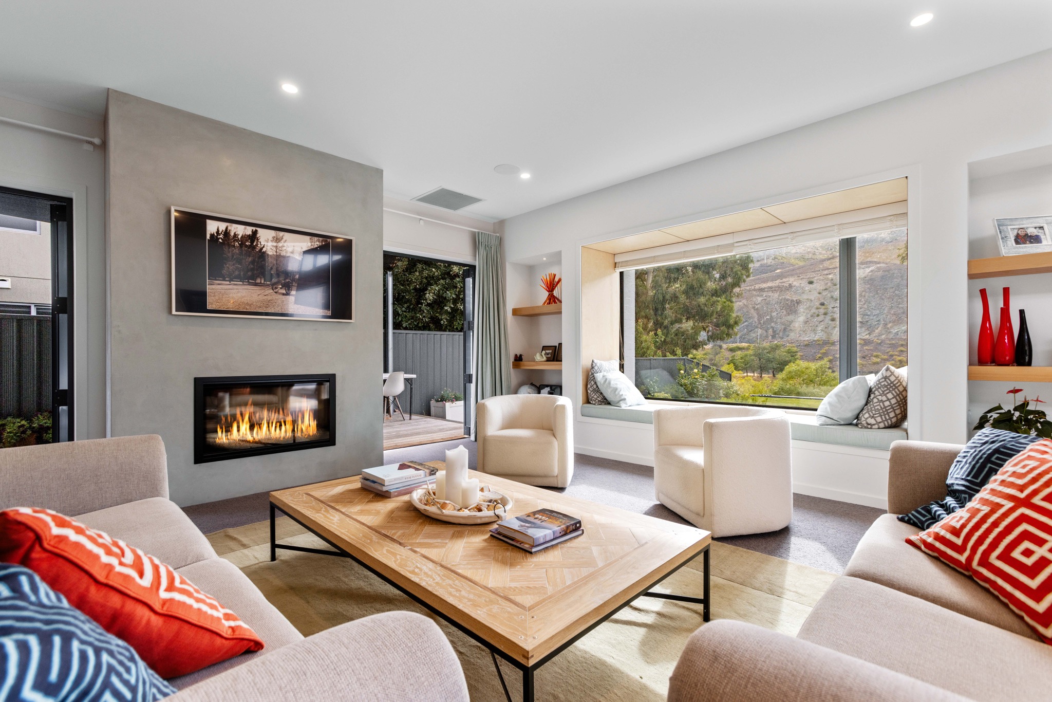 Bright living room with a fireplace, neutral sofas and a window seat overlooking hills