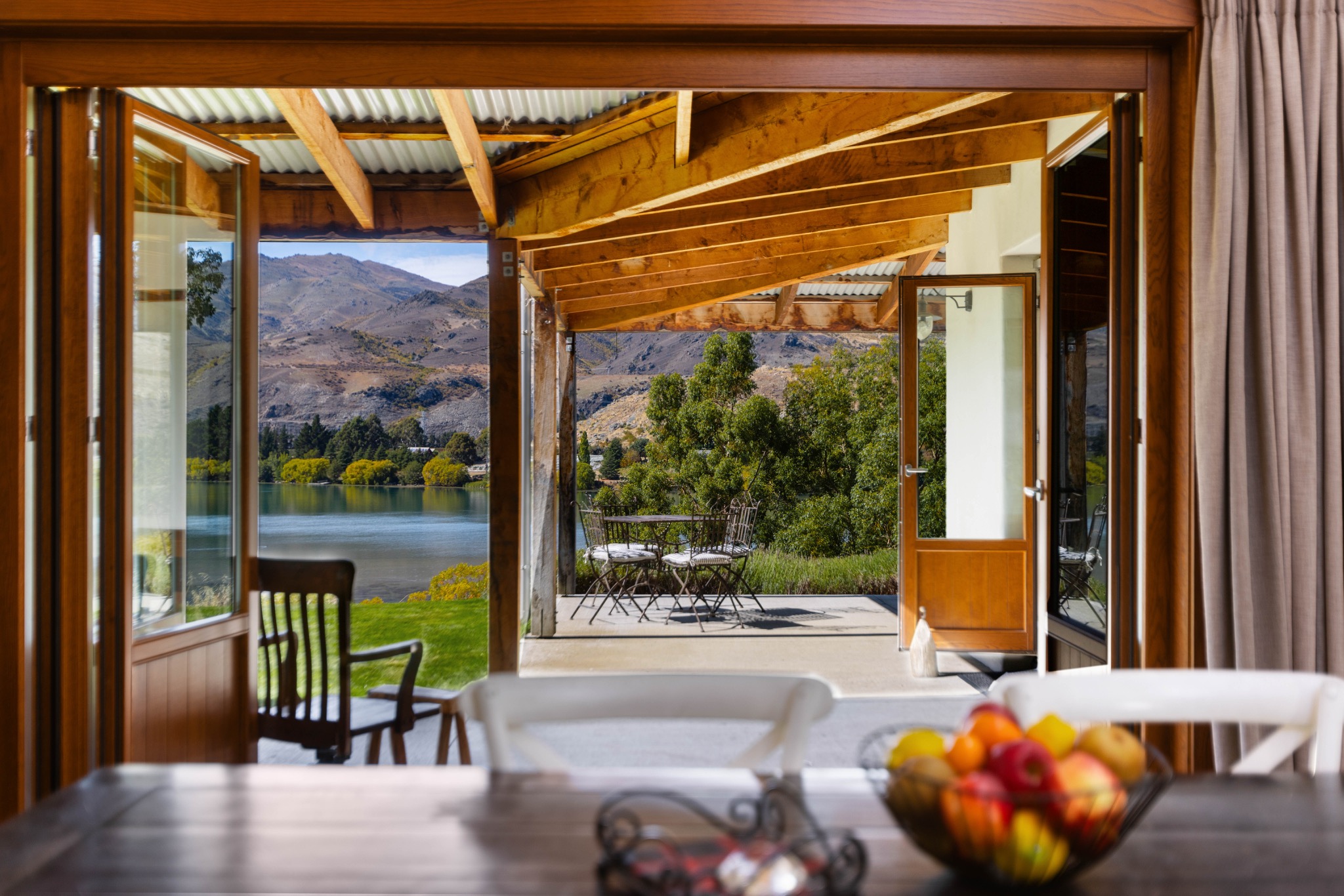 View through open timber doors to a covered terrace and lake and mountains
