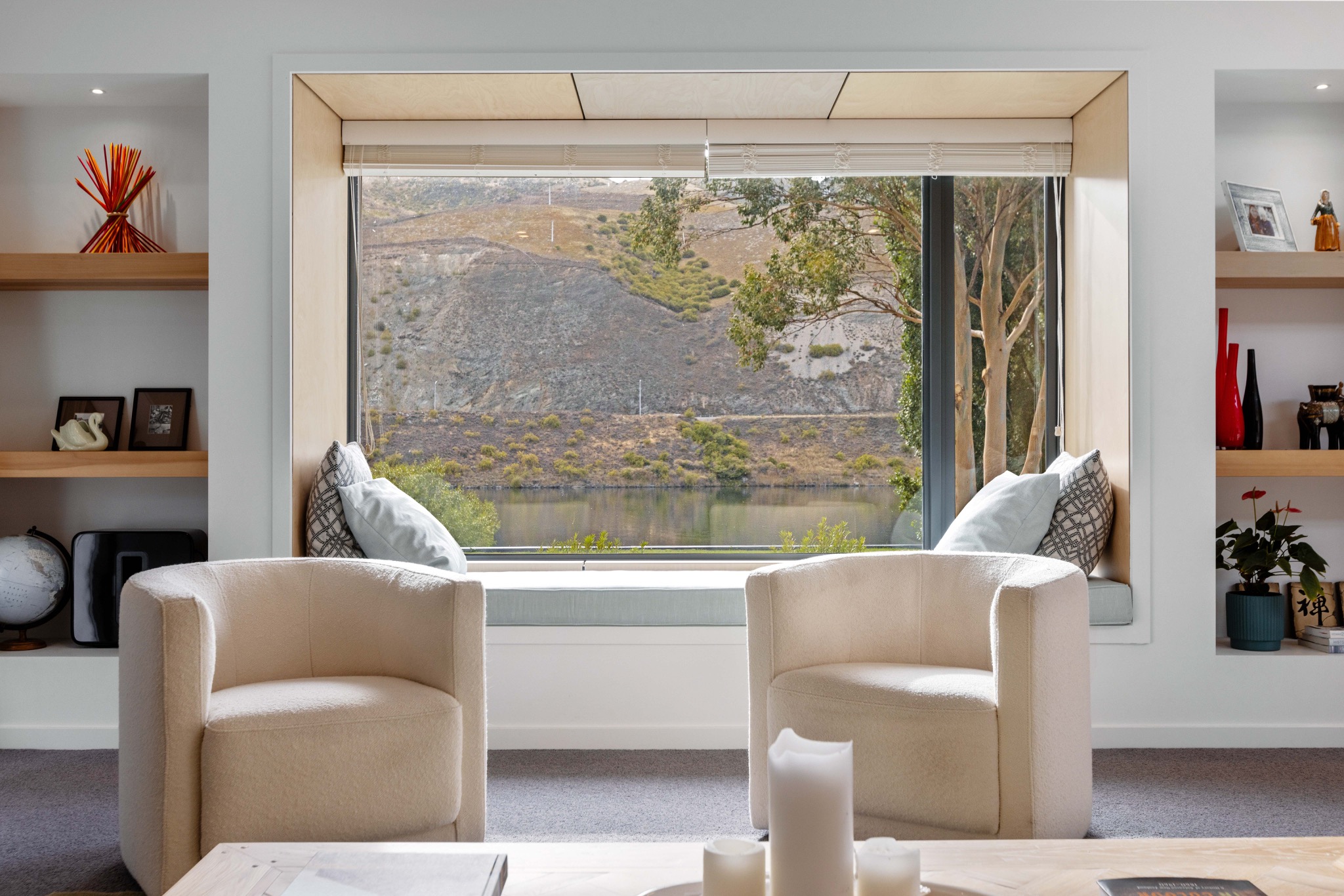Cream armchairs beside a picture window overlooking water and hills